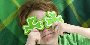 rothaariges und sommersprossiges Gesicht irischer Junge Kobold mit Shamrock-Plätzchen über den Augen lächelndes irisches Kind mit grünem St. Patricks-Hintergrund