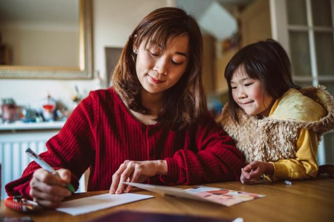 Junge hübsche Mutter, die zu Hause mit ihrer schönen Tochter eine Grußkarte für die Familie schreibt