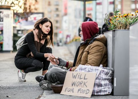 Junge Frau, die dem obdachlosen Bettlermann sitzt in der Stadt Geld gibt.