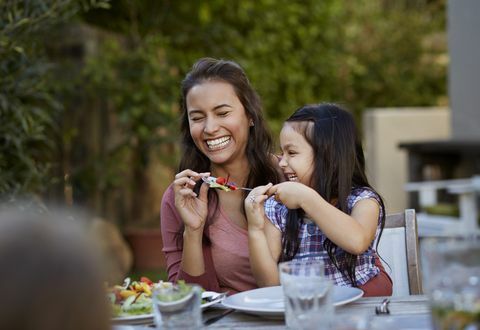 Mädchen, das versucht, ihre Mutter beim Abendessen draußen zu füttern, während es lacht