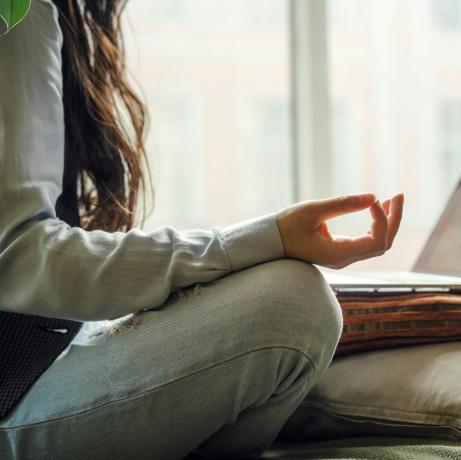 Eine asiatische Frau mittleren Alters in blauen Jeans sitzt in Yoga-Pose vor einem Laptop auf dem Bett und arbeitet zu Hause online beim Online-Shopping in der Quarantänezeit