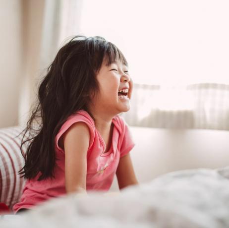 Kleines Mädchen lacht fröhlich im Bett