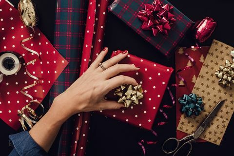 Frau, die Weihnachtsgeschenke einwickelt, präsentiert Foto, das von oben über Kopf genommen wird. Hände wickeln Papierbögen Tischplatte direkt über