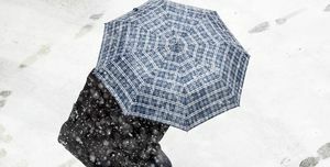 Hochwinkelansicht einer Person mit Regenschirm, die im Schnee auf der Straße läuft, mit rotem Regenschirm im Schneesturm. Valencia, Spanien