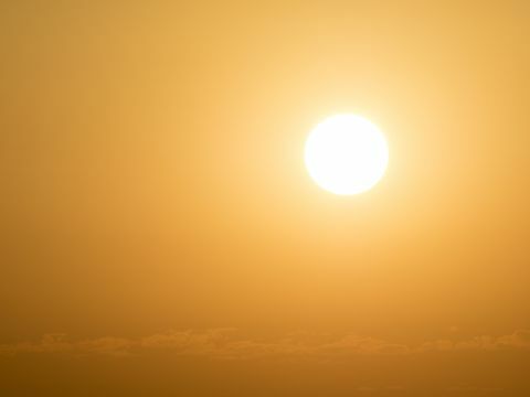 Glühende Sonne des vollen Rahmens bei Sonnenuntergang mit einem orange und gelben Himmel