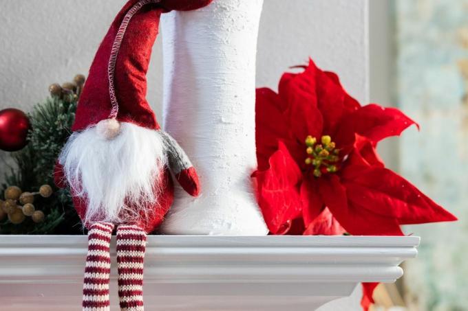 Eine klassische norwegische Weihnachtszwergdekoration, die auf einem weißen, modernen Kaminsims mit einer weißen Vase mit Eukalyptus und einer Weihnachtssternblüte sitzt