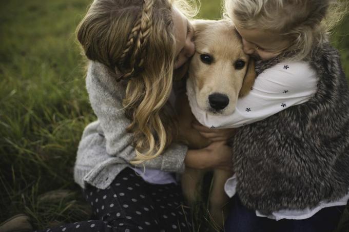 Zwei junge Mädchen umarmen ihren Hund im Freien