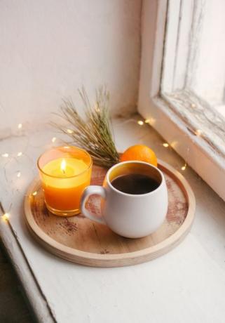 gemütliche winterhausinnendetails, tasse kaffee, holztablett, mandarinen- und kerzenfensterbankstillleben für weihnachten