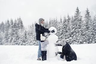 Dreiköpfige Familie baut einen Schneemann im Schnee