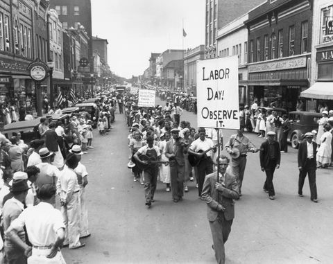 Parade zum Tag der Arbeit im Jahr 1934 mit Menschen, die auf die Straße gehen, während sie Schilder halten, während eine Menge von den Bürgersteigen aus zusieht