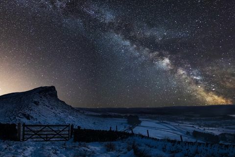 Zusammengesetztes Bild der lebendigen Milchstraße über der Landschaft des schneebedeckten Peak District-Nationalparks in England