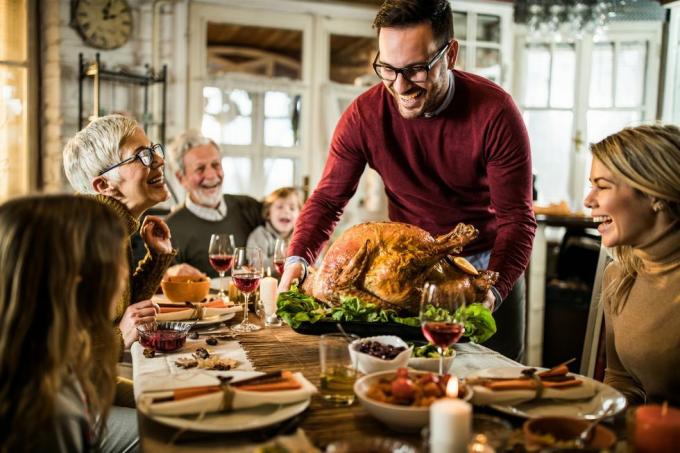 Glücklicher Mann, der seiner Familie während des Thanksgiving-Abendessens am Esstisch gebratenen Truthahn serviert