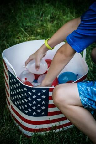 Kind, das kleine rote, weiße und blaue Wasserballons aus der Wanne mit amerikanischer Flagge darauf auswählt