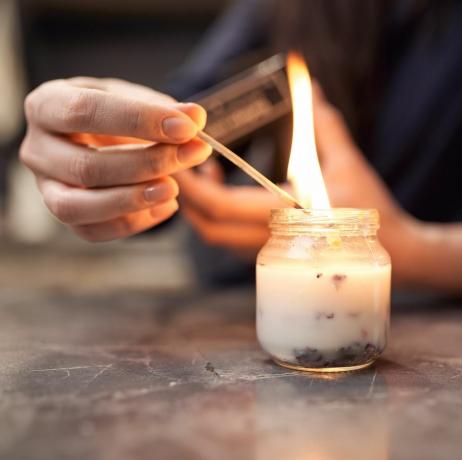 Ernte anonyme Frau mit brennendem Streichholz, das eine aromatische Kerze im Glas anzündet, die zu Hause auf einem Marmortisch platziert ist