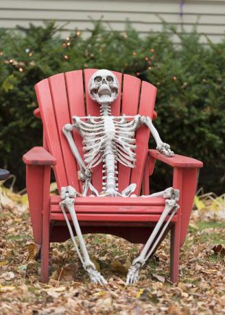 glückliches Skelett, das auf einem Stuhl sitzt