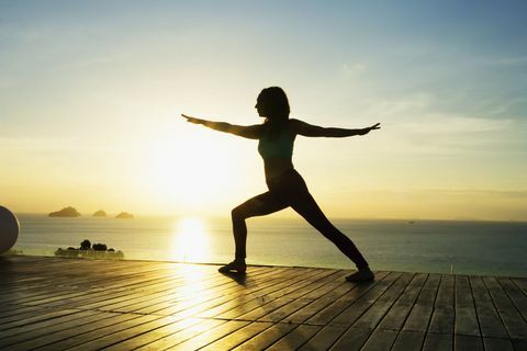 Frau macht Yoga am Meer bei Sonnenuntergang