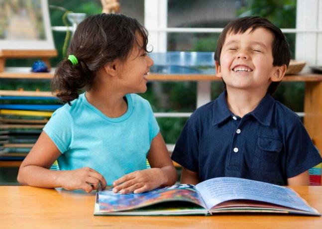 Zwei lachende Kinder, die in der Schule ein Buch lesen