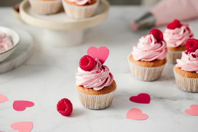 Frisch zubereitete Himbeer-Cupcakes auf der Küchentheke. Köstlich aussehende rosa Cupcakes mit Himbeer- und Papierherz-Topping