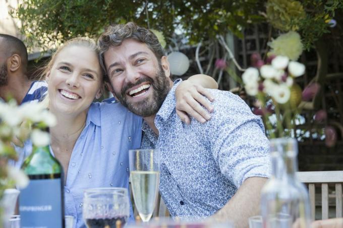 Lachendes Paar beim Mittagessen mit Freunden auf der Gartenterrasse