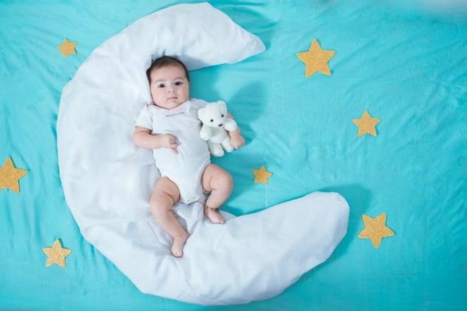 Schönes lateinamerikanisches Mädchen, zwei Monate alt, auf einem weißen Laken in Form eines Mondes mit gelben Sternen auf jeder Seite und einem blauen Laken darunter liegend