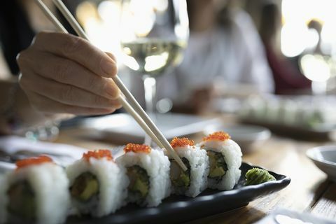 Frau mit den Essstäbchen, die für Sushi auf Restaurantbehälter erreichen