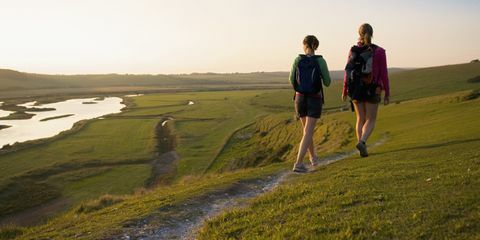 Zwei Frauen, die auf einem Hügel in Richtung zum Sonnenuntergang wandern