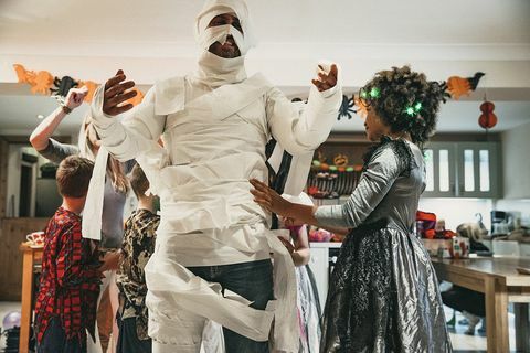 Eine Gruppe von Kindern, die einen ihrer Eltern in Toilettenpapier kleiden, um auf einer Halloween-Party wie eine Mumie auszusehen
