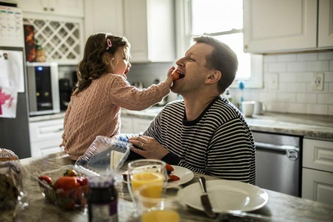 Kleinkindmädchen füttert ihren Vater in der Küche mit einer Erdbeere