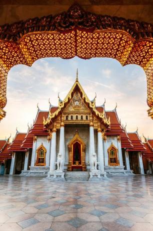 Sonnenaufgang am Marmortempel, Thailand mit einem Äußeren aus goldenen Bögen und Fluren, weißen Marmorsäulen und einem geometrisch gekachelten Marmorhof