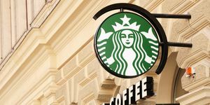 wien, österreich 1. mai 2012 grünes starbucks-kaffeelogo auf einer stange und starbucks-kaffeetext auf fassade von ein altes haus in wien mitte schräg fotografiert fokus auf logo starbucks ist bekannt für große to go Kaffee