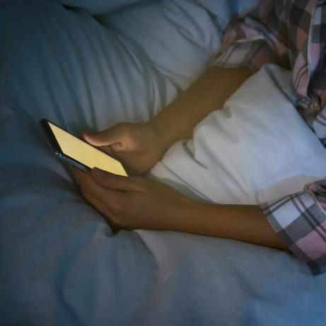 Frau benutzt nachts Smartphone im Bett, Nahaufnahme, Nomophobie und Schlafstörungen