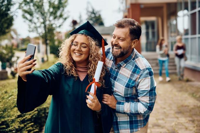 glückliche universitätsabsolventin und ihr vater haben spaß beim selfie mit dem smartphone