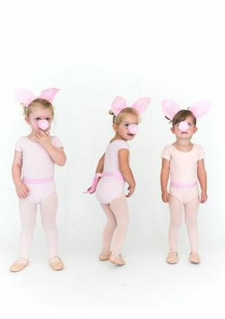 kleine Mädchen in rosa Strumpfhosen und Onesies mit Schweineohren und Schweineschnauzen