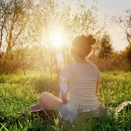 Junge Frau sitzt in Yoga-Position und genießt den Sonnenuntergang in der Natur