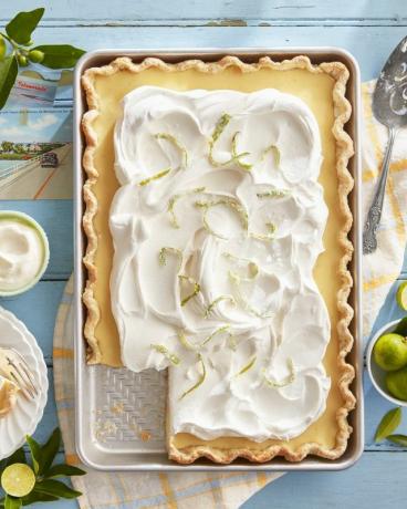 Key Lime Slab Pie in einem Backblech auf einem blauen Tisch mit Schlagsahne und kandierter Limette obendrauf