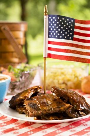 Grillrippen mit amerikanischer Flagge, Bohnen, Kartoffelsalat auf einem rot-weißen Tischtuch