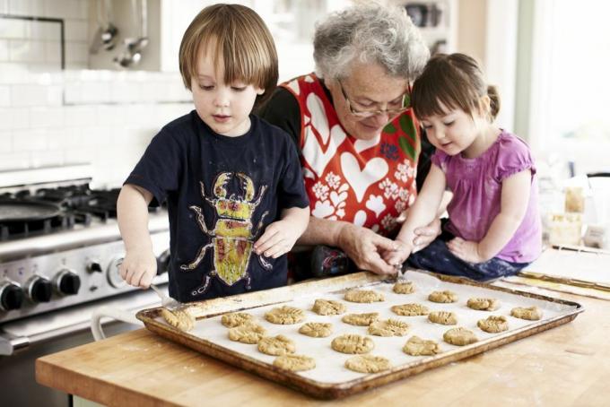 Oma und zwei kleine Enkelkinder backen. Die Enkelin legt mit Hilfe der Großmutter Teig auf ein Backblech