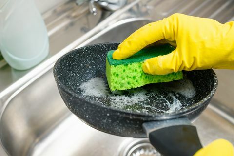 Hand mit einem Schwamm wäscht eine schmutzige Pfanne unter fließendem Wasser