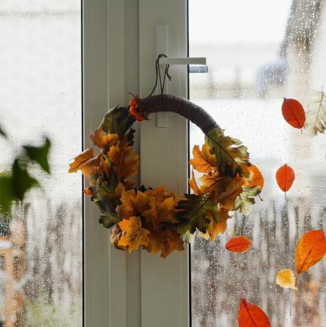 DIY-Herbstkranz aus bunten roten, braunen und gelben Blättern am Fenster an einem regnerischen Herbsttag