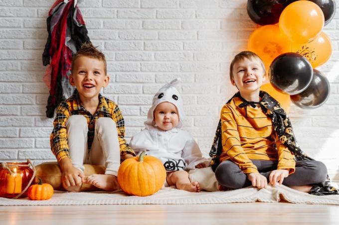 kinder in kostümen feiern halloween weiße backsteinmauer mit dekorationen kopierraum