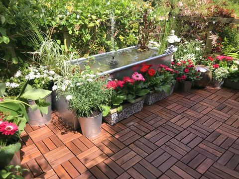 Stock Foto von Garten Baumhaus Terrasse Plattform Balkon im Sommer mit Zink Metall Trog Teich Wasserspiel mit Solarbrunnen Pumpe, Goldfischfische, Randpflanzen, rote Miniaturrosen, rosafarbene Gerberablumen, Teakdeckplatten, solarbetriebene Lichter, Beleuchtung